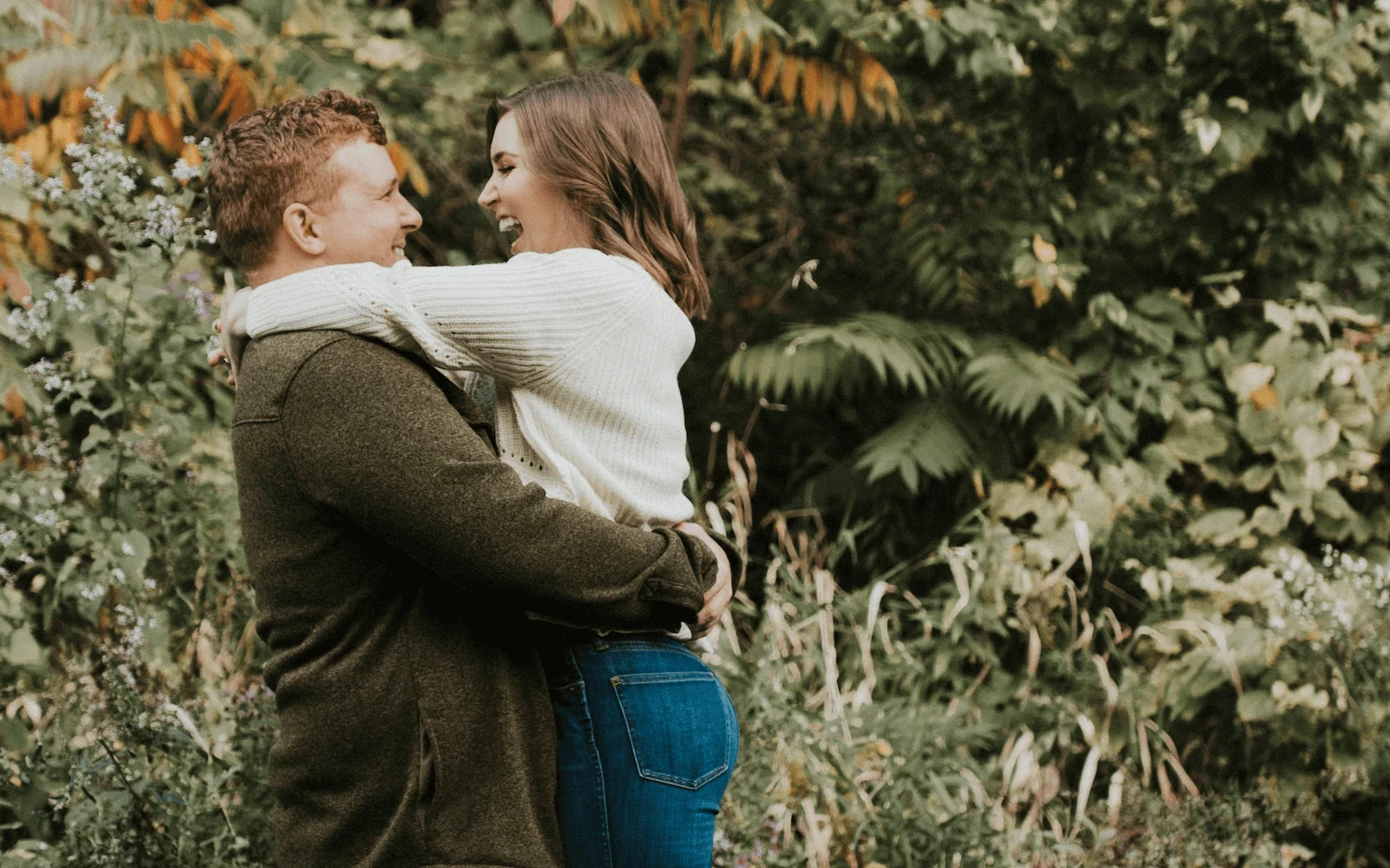 An engaged couple holding hands among trees